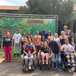 VÁRIAS PESSOAS, HOMENS E MULHERES, EM FRENTE UM PAINEL DE LONA COM ESTAMPAS DE NATUREZA, EM CIMA DE UM GRAMADO. ATRÁS DO PAINEL TEM O TOPO DE UMA ARVORE E SE VÊ PARTE DO TELHADO E VARANDA DE UMA CASA DE EVENTOS. AS PESSOAS ESTÃO EM PÉ, LADO A LADO E NA FR