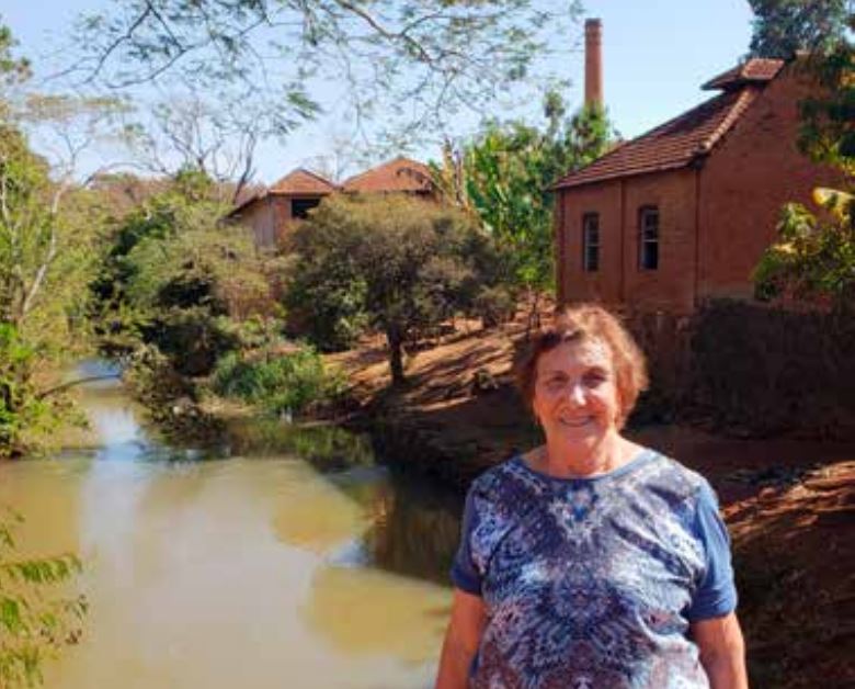 (Jandyra Mattioli Lázaro as beiras do Córrego Rico e ao fundo a sede do Curtume e sua famosa Chaminé que existe até os dias atuais).